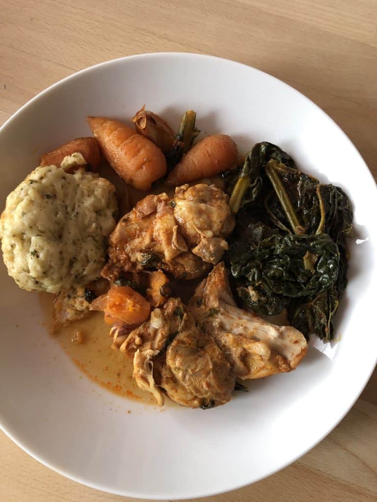 Instant Pot Chicken Stew with Dumplings on a white plate. Chicken thigh fillet, cavolo nero, carrot and dumpling. Wooden table as background