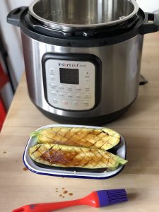 The halved and scored aubergine with an Instant Pot Duo Crisp behind it and a red and purple silicone brush in front of it, it's been drizzled with sauce