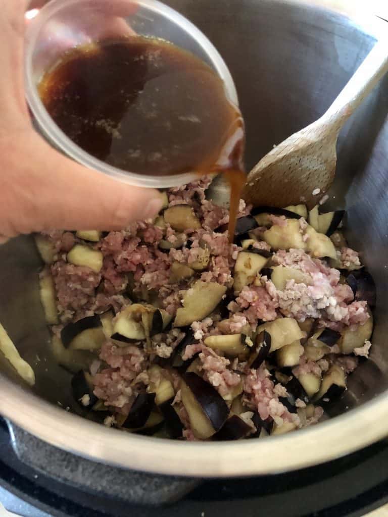 Photo showing a hand holding a cup and pouring oyster sauce ont o the mince and aubergine