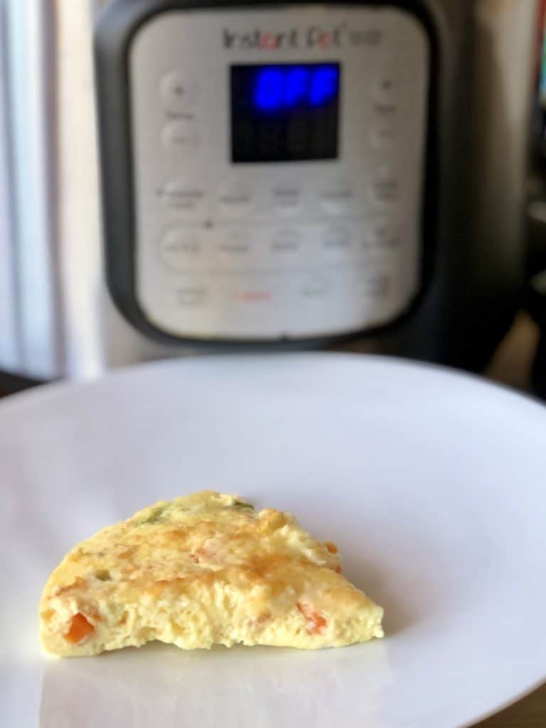 Photo of a slice of Feisty Tapas Duo Crisp Crustless Quiche on a white plate with Instant Pot in background
