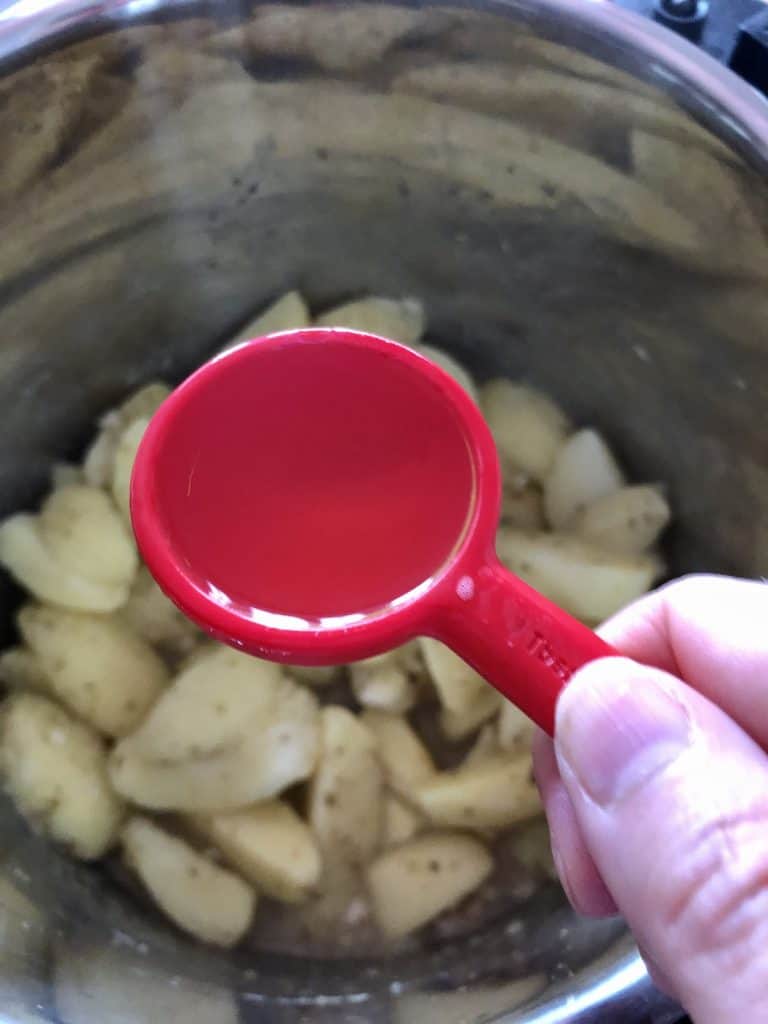 Photo of a red measuring spoon being held above the raw potato wedges