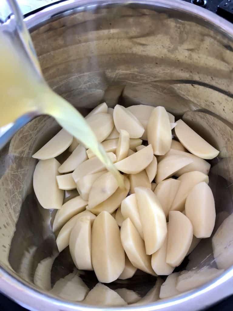 Photo of the raw potato wedges inside the inner pot, stock is being poured on them from the top left