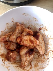 Photo of a white mixing bowl with the raw chicken wings smothered in bbq sauce ready to air fry