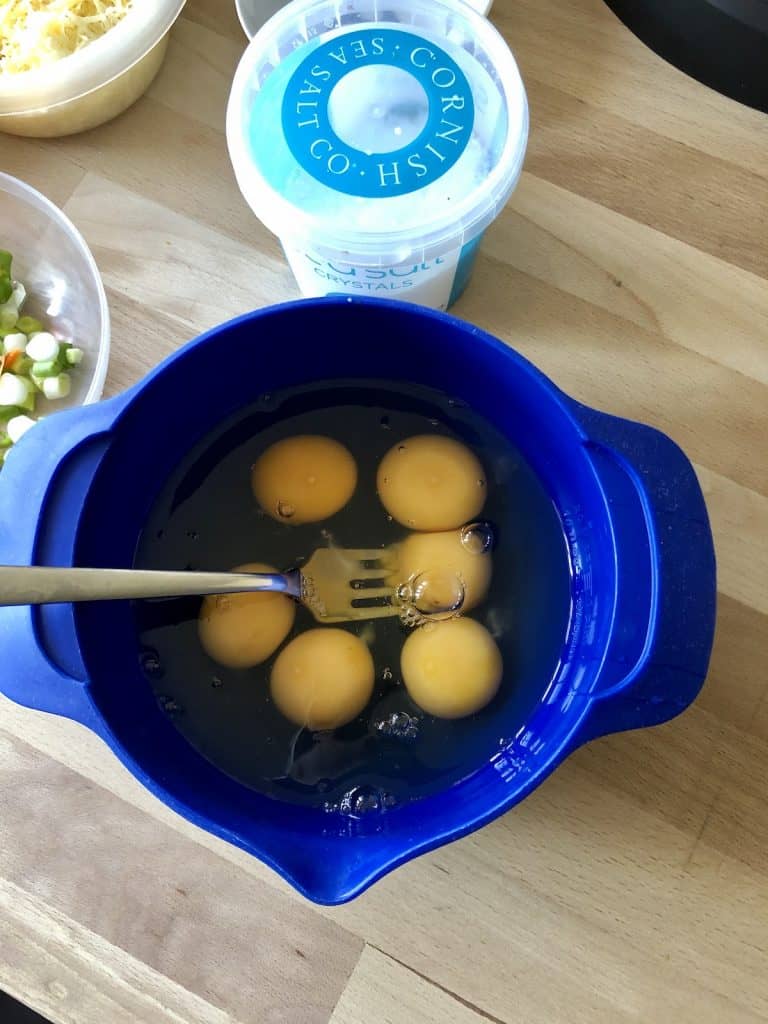 Photo from above of the eggs inside a blue Joseph Joseph mixing bowl, a fork rests on the left side of the bowl and there is a tub of sea salt at the top of the photo