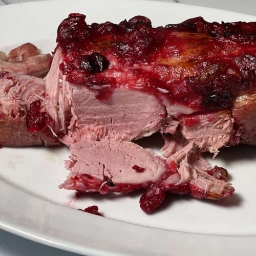 The Cranberry Sauce-Glazed Gammon joint on a white plate with a slice in front of it