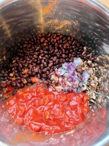 Chopped mushrooms, paprika, cumin, red onion, black beans and chopped tomatoes in Instant Pot's stainless steel inner pot - seen from above