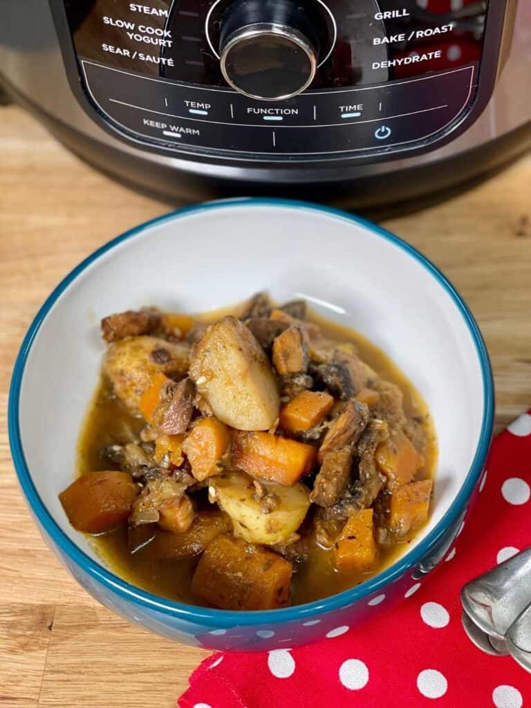 Photo of the Vegan mushroom stew with a red and white polka dot napkin and the Ninja Foodi multi cooker in the background, on a wooden board