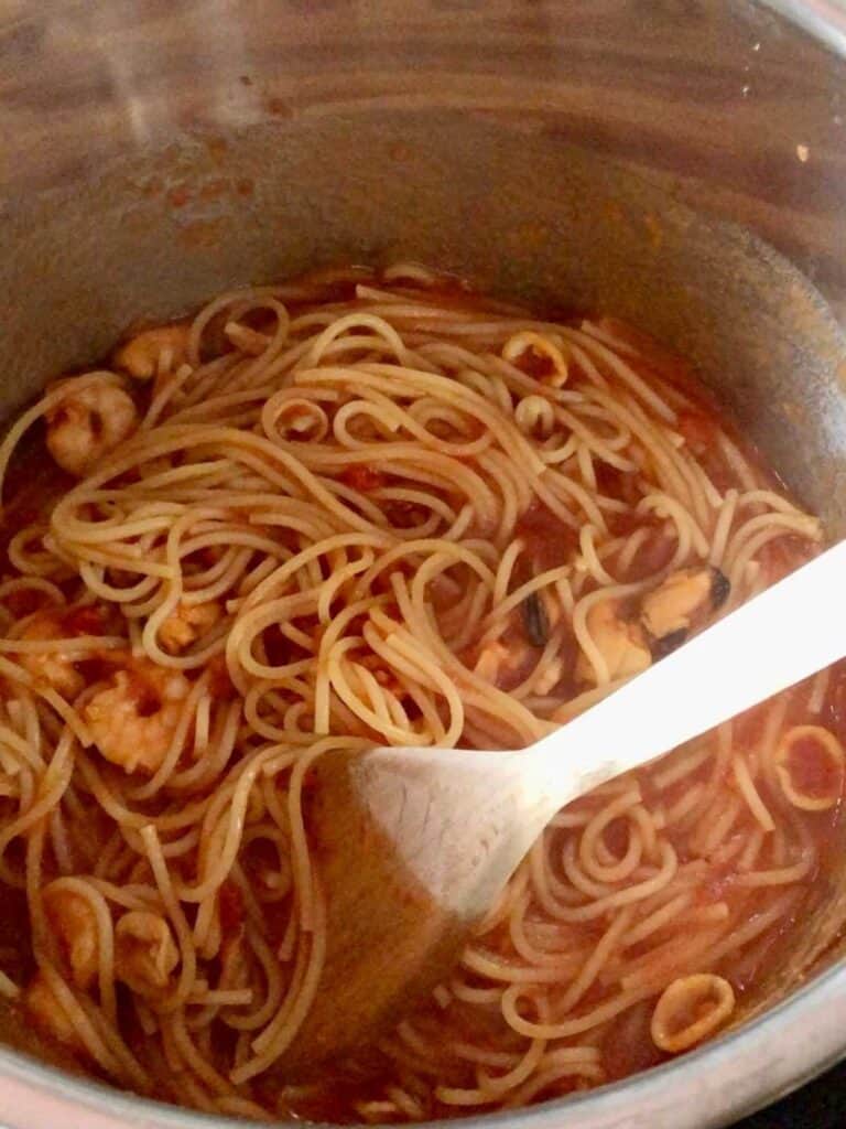 Mixed seafood spaghetti after pressure cooking seen from above with a wooden spoon in the Instant Pot's stainless steel inner pot