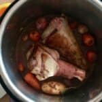 Photo of Lamb shanks seen from above inside the Instant Pot's stainless steel inner pot, with the potatoes and carrots showing underneath