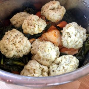 Photo of the pressure cooked chicken and vegetables topped with dumplings is seen from above still inside the stainless steel inner pot of the Instant Pot, on a light wooden surface