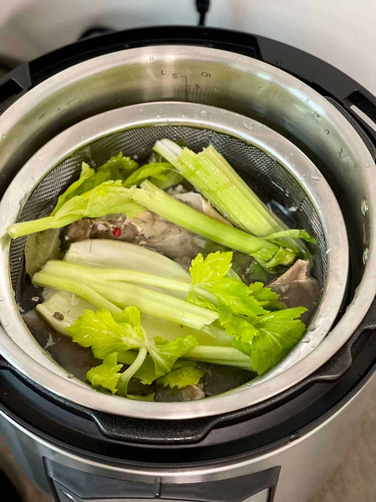 All ingredients for pressure cooker turkey stock placed inside a sieve inside the inner pot of an Instant Pot Duo Evo Plus - seen from above