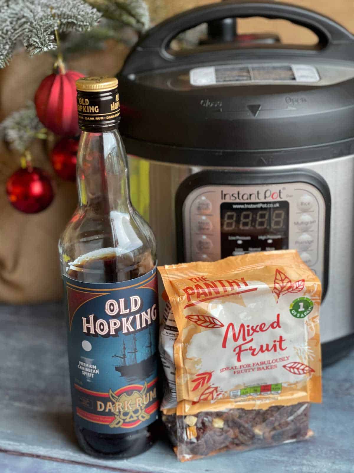 Bag of dried fruit and bottle of dark rum (both from Aldi) in front of an Instant Pot Duo with Christmas tree and red baubles in the background