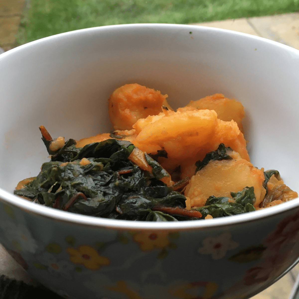 Instant Pot pressure cooked Paprika Chard and Potatoes in a light blue bowl with flowers and white inside. There's grass in the background