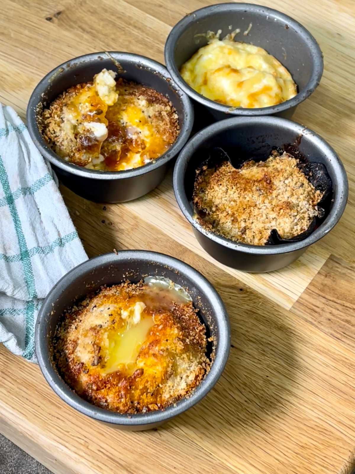 Air fried egg pots seen from above on a wooden chopping board with a white and green tea towel on the left