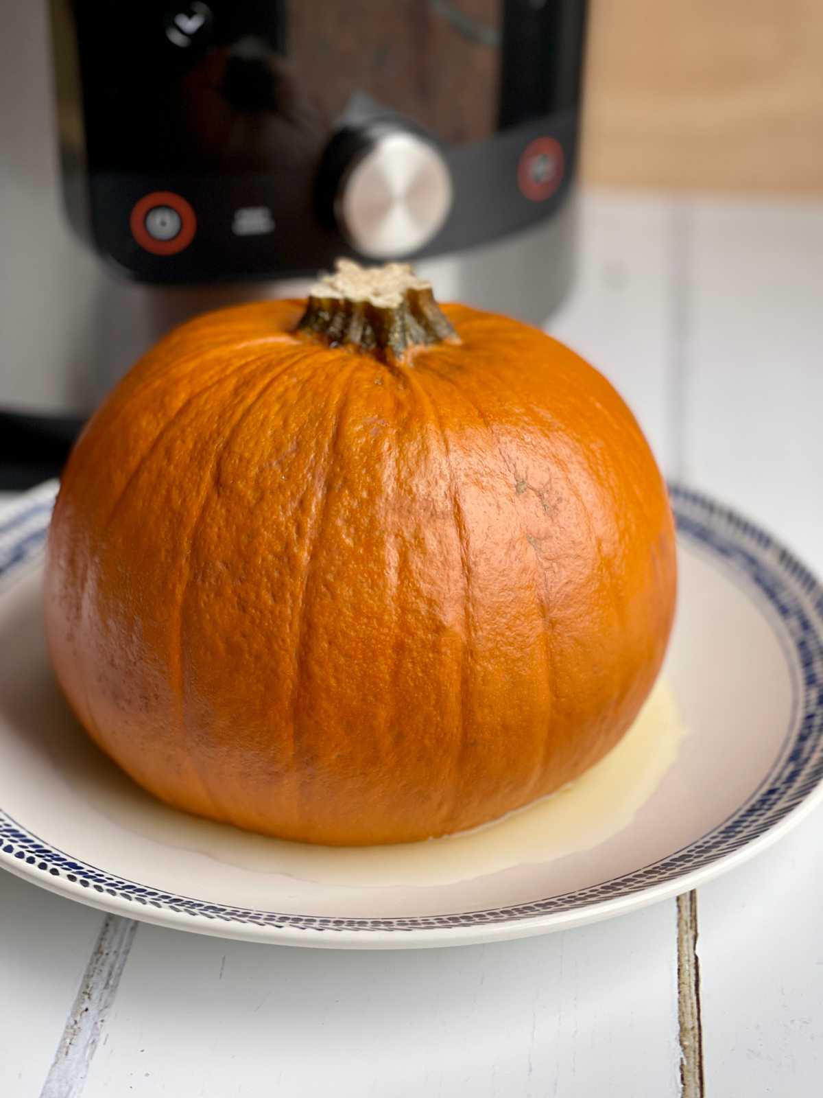 Photo of a pumpkin on a white plate with pressure cooker in the background