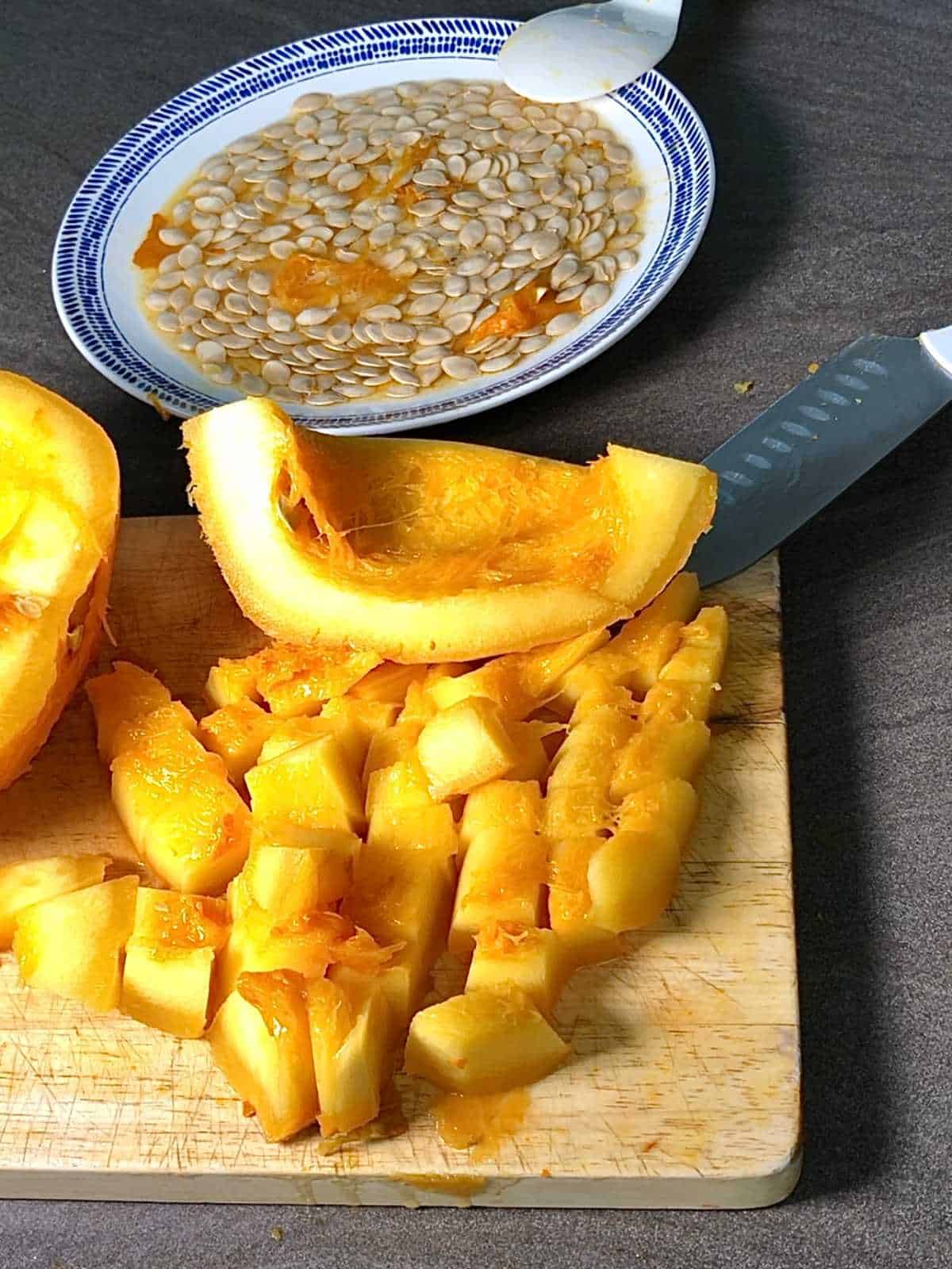 Photo of a pressure cooked instant pot pumpkin effortlessly diced on a chopping board, with the seeds seen on a plate in the background