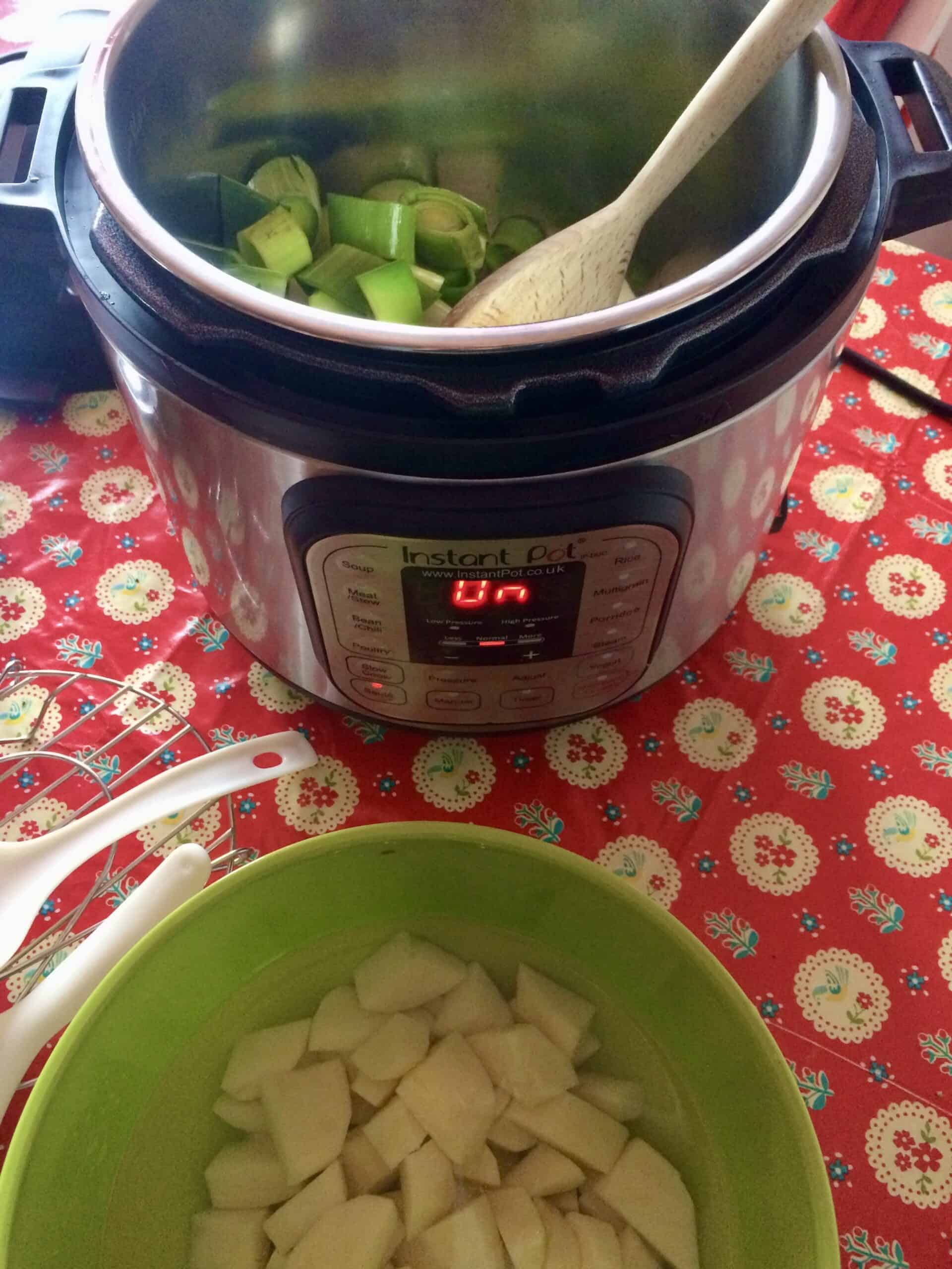 Photo of the Instant Pot Duo electric pressure cooker sautéing the leeks, with the bowl of chopped up potatoes on show too