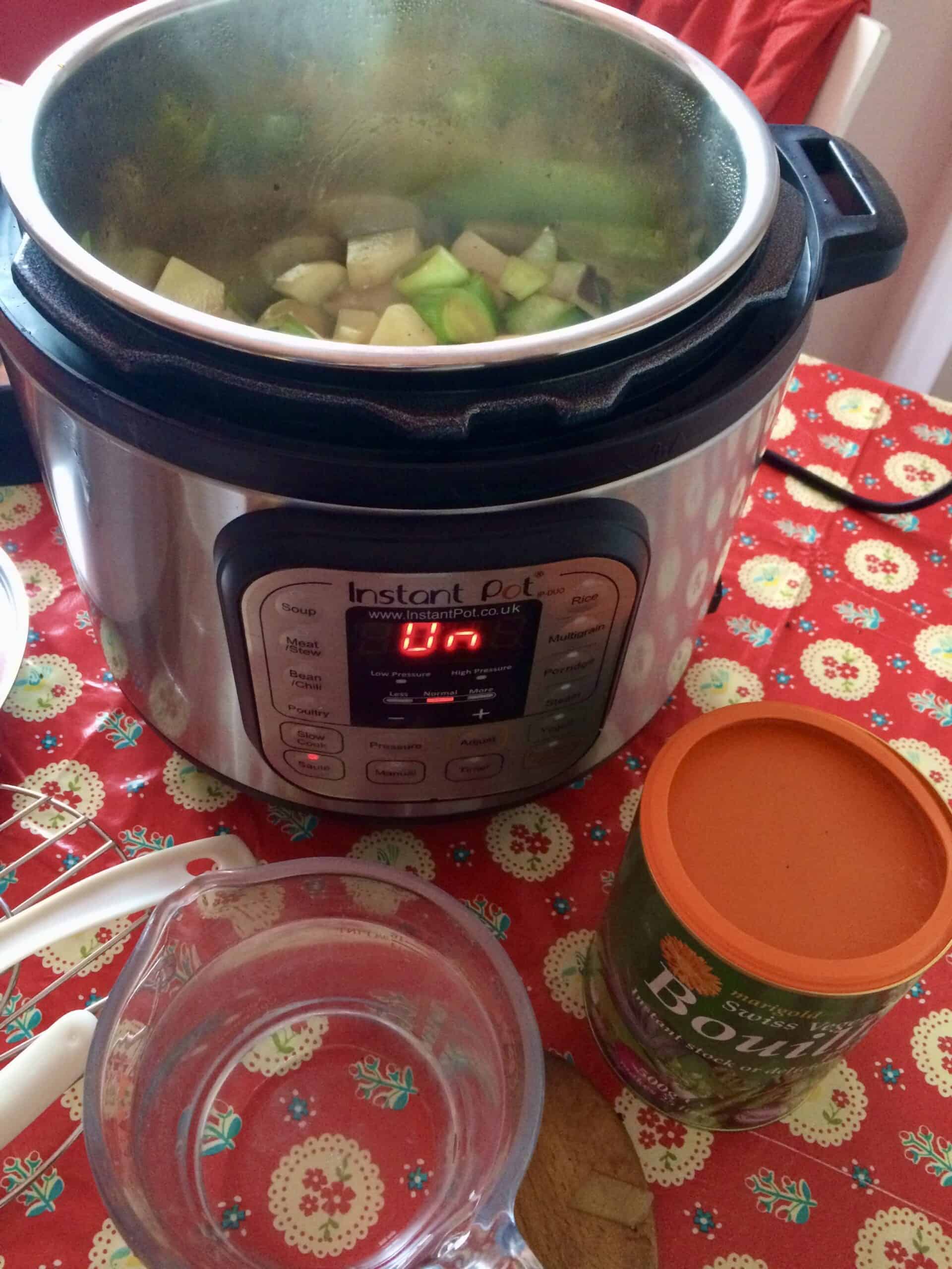 Photo of the leeks and potatoes sautéing in the Instant Pot Duo electric pressure cooker with a tub of Bouillon and a pyrejx jug with water showing