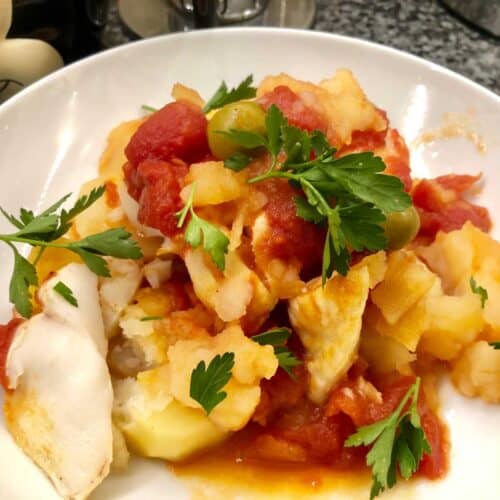 The pressure cooked fish stew with olives and potatoes served on a white plate and sprinkled with fresh parsley