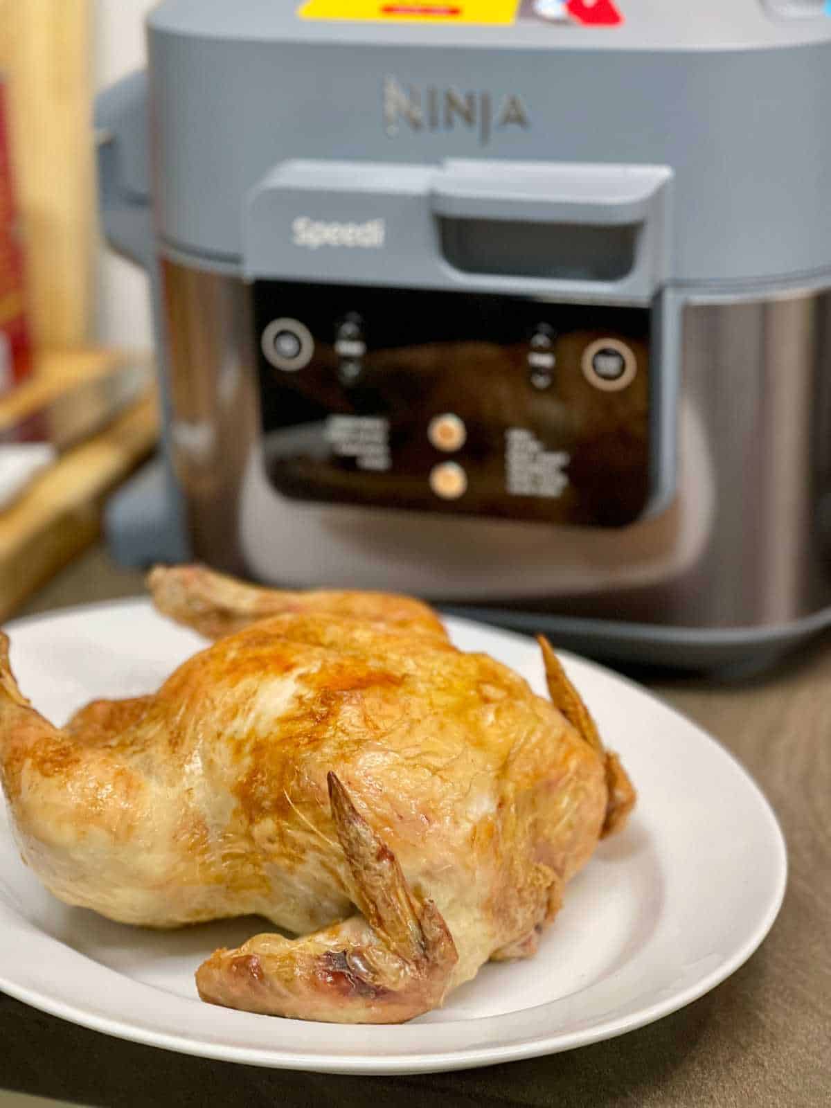 Photo of a crispy whole roasted chicken seen in front of a Ninja Speedi 10 in 1