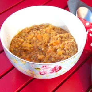 Spanish lentejas lentil stew seen in a pretty blue flowery bowl, with a red slatted table as the background