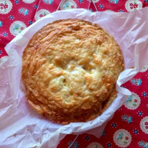 The cheesy chorizo crustless quiche from above resting on scrunched greaseproof paper, on a colourful red tablecloth with a pattern of birds, doilies and flowers