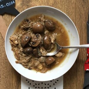 The pressure cooked Chicken and Mushroom seen on a white plate, a stainless steel spoon rests on it too with the handle pointing to the right