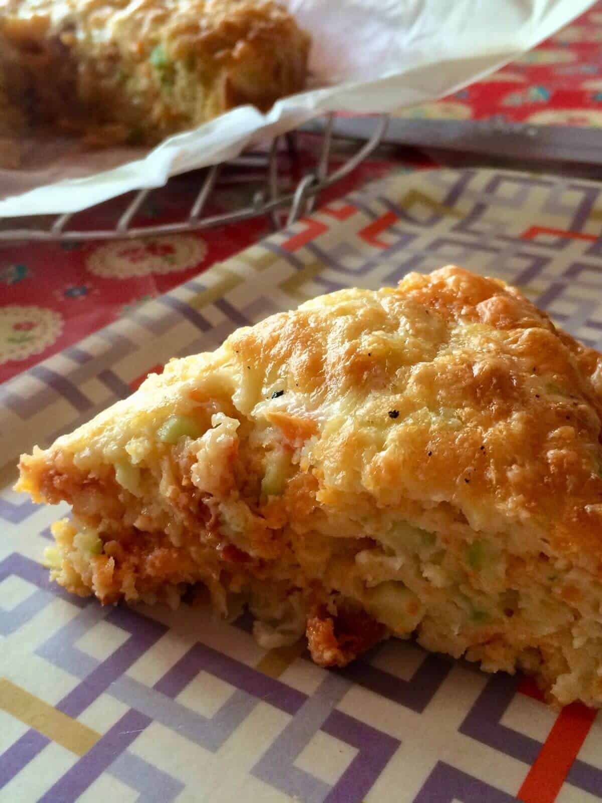 Photo of a slice of cheesy chorizo crustless quiche showing the chopped up vegetables and chorizo and with a cheesy crust, the rest of the quiche can be seen in the background