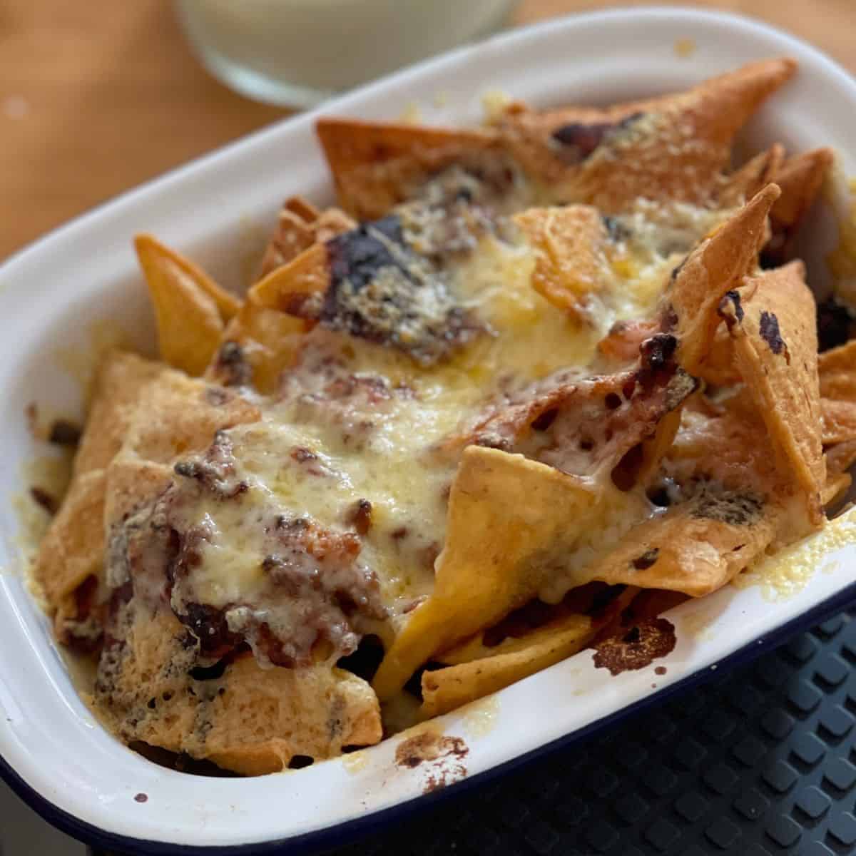 Photo of a white rectangular enamel dish full of cheesy loaded nachos