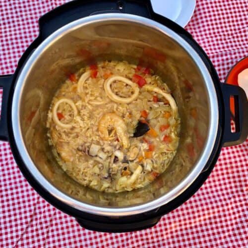 The seafood rice seen from above inside an Instant Pot Duo, against a red and white gingham tablecloth