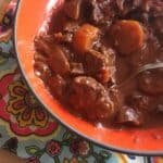 A photo of the Instant Pot Chocolate Beef Stew in an orange bowl with a colourful tea towel underneath