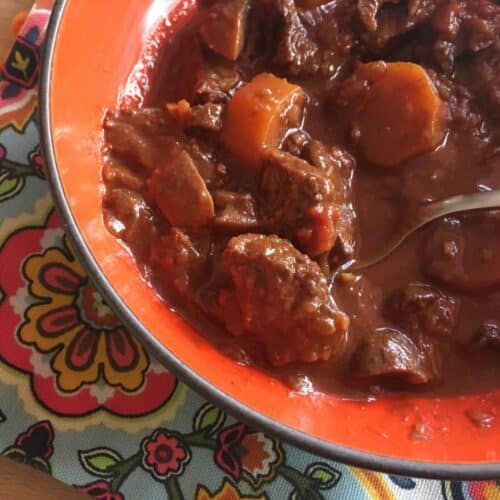 A photo of the Instant Pot Chocolate Beef Stew in an orange bowl with a colourful tea towel underneath