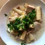 The delicious Chicken and Pancetta Rigatoni seen from above surrounded by sauce on a white plate and topped with fresh parsley