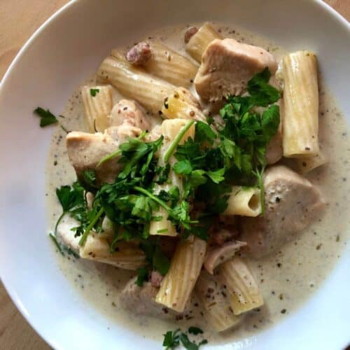 The delicious Chicken and Pancetta Rigatoni seen from above surrounded by sauce on a white plate and topped with fresh parsley