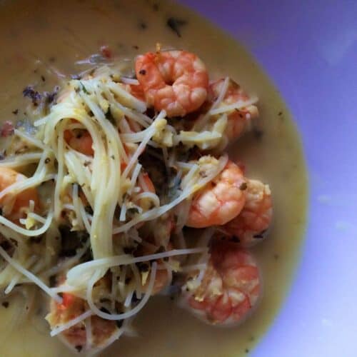 The noodles and prawns surrounded by delicious broth seen from above on a white plate
