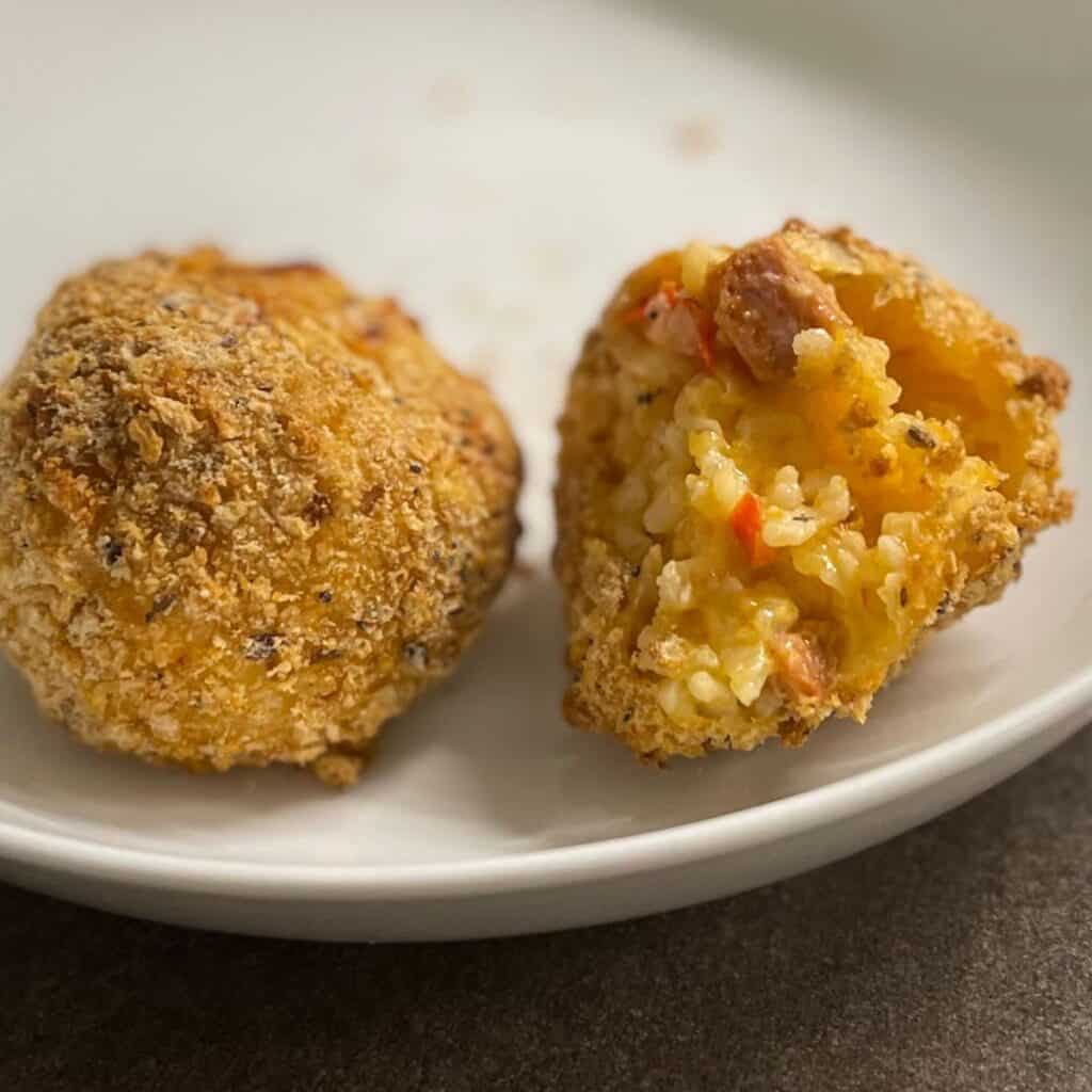 Two air fried Arancini Rice Balls made with Chorizo Risotto. The ball on the right has a bite taken out showing the chorizo and rice inside