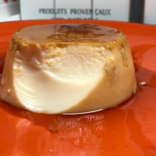 A pressure cooked flan de Huevo served on an orange plate, one bite has already been eaten so the smooth inside is showing, there's delicious caramel too