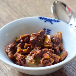 A white bowl with blue motifs containing lime pickle, there's a spoon on the top right of the image