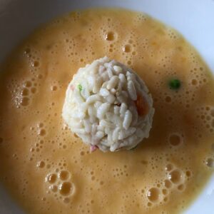 A golf-sized arancini rice ball just before coating in the beaten egg in which it sits