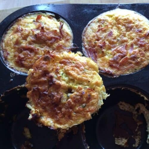 Three Thermomix Ham Hock Egg Muffins, two are still inside the muffin tin and one is propped on it