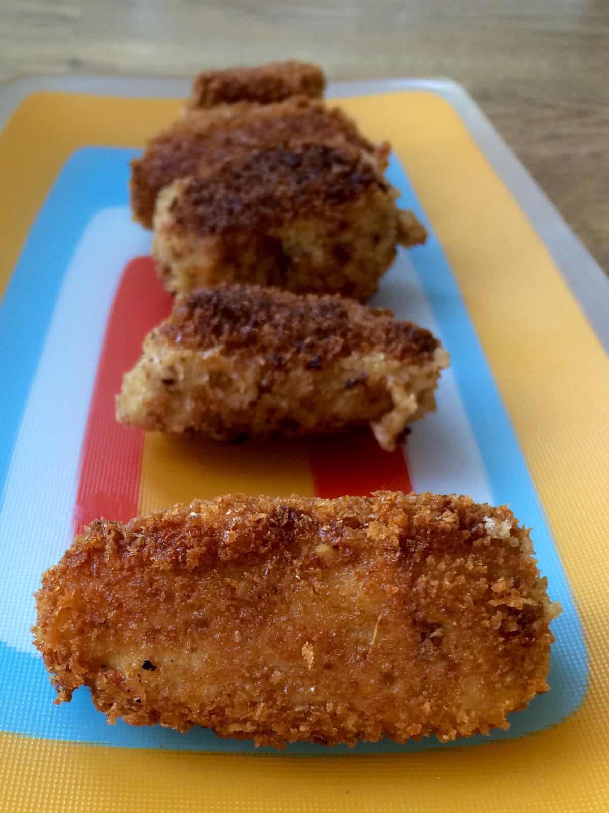 A row of five croquettes on a colourful plate